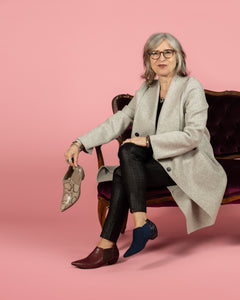 Designer Elena Brennan holding Tan Snakeskin bootie and Blue suede and leather bootie wearing Blue and Oxblood booties